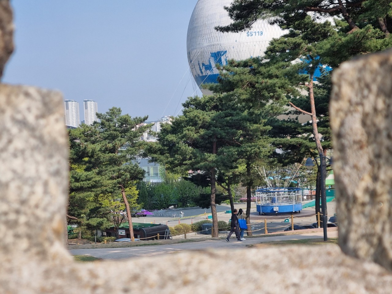 18일 오후 4시40분께 수원시 팔달구 행궁동에 있는 창룡문 성곽 사이로 보이는 한 가족이 플라잉수원 헬륨기구를 타러 가는 듯 발길을 재촉하고 있다. (사진=권영복 기자)