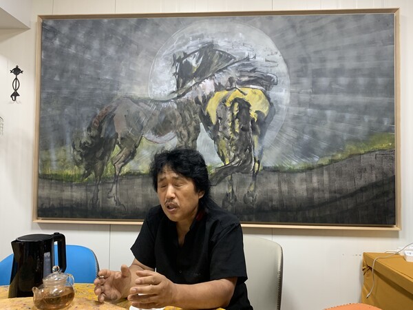 눈을 지긋이 감은 채 두 손으로 감정을 표현하는 홍승표 작가가 뒤의 그림에 대해 "우주에서 어머니를 만나는 어미말과 새끼말을 나타낸 그림"이라고 말하고 있다./사진=오기춘 기자
